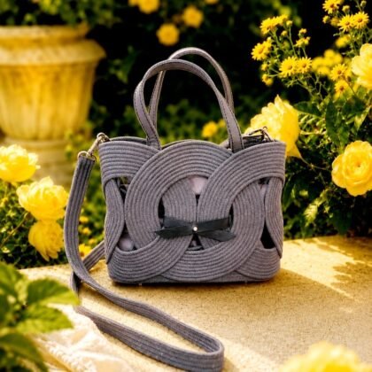 Gray Infinity woven handbag with leather handles in outdoor garden setting Sculptural gray handbag with infinity woven front design Gray boutique handbag with removable crossbody strap and lined interior Side view of gray structured woven handbag with protective feet Infinity Collection gray handbag styled as shoulder and crossbody bag