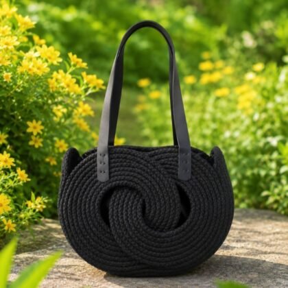 Infinity Collection black woven handbag with double leather shoulder straps Sculptural black woven shoulder bag with circular detail Black woven handbag with lined interior and leather straps Boutique black statement handbag styled outdoors