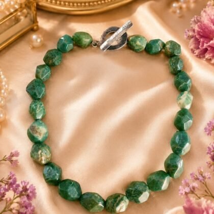 Faceted green semi-precious stone necklace with natural cream and moss-toned variation styled on neutral surface