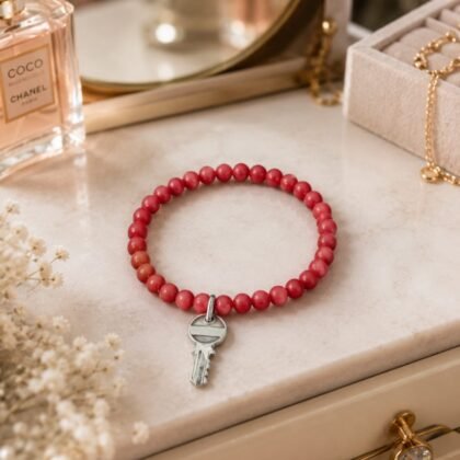 Red beaded unisex stretch bracelet with silver-tone key charm displayed in a clean minimalist jewelry setting.
